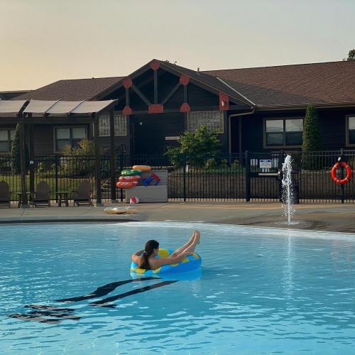 A person relaxes on a float in a pool, with a sunny sky and a building in the background.