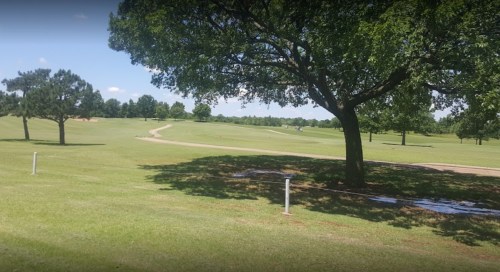 A sunny golf course with a winding path, trees, and lush green grass under a clear blue sky.
