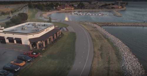 Aerial view of a waterfront area with a restaurant, marina, and a winding road along the shore.