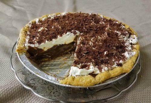 A chocolate cream pie with whipped cream topping and chocolate shavings, partially sliced on a decorative plate.