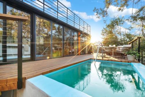Modern deck with a small pool, surrounded by trees and sunlight, featuring outdoor seating and large glass doors.