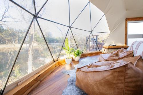 Cozy interior of a geodesic dome with bean bags, plants, and large windows overlooking a natural landscape.