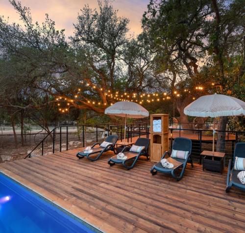 A serene outdoor space with lounge chairs, umbrellas, and string lights near a pool, surrounded by trees at sunset.