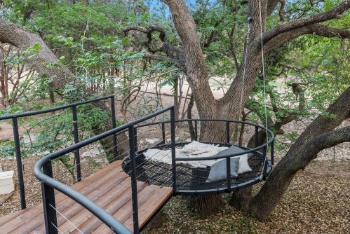 A cozy hanging bed on a tree platform, surrounded by greenery and a wooden walkway.