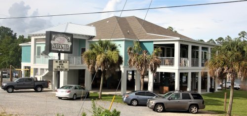 A two-story teal building with palm trees, featuring a sign for "Steamer" and parked cars in front.