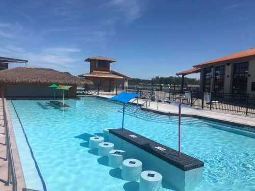 A sunny pool area featuring colorful umbrellas, a thatched roof cabana, and lounge chairs by the water.