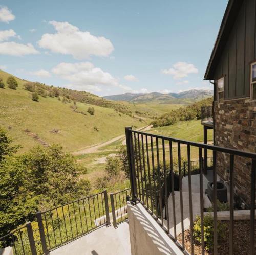 A scenic view of rolling hills and mountains from a balcony, with a clear blue sky and scattered clouds.