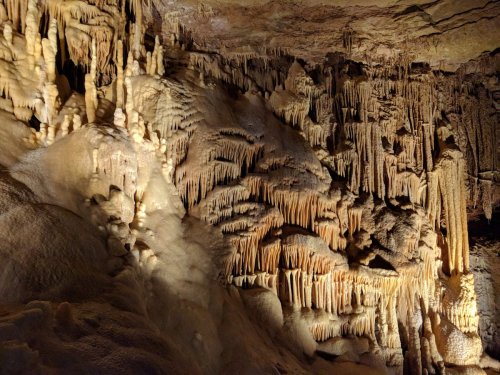 Stalactites and stalagmites in a dimly lit cave, showcasing intricate rock formations and textures.