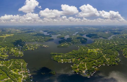 Aerial view of a lush, green landscape with winding waterways and scattered homes under a blue sky with fluffy clouds.