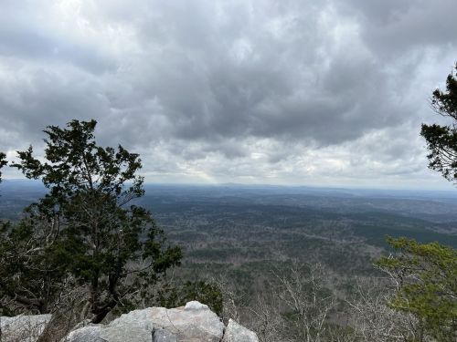A panoramic view from a rocky outcrop, showcasing a vast landscape under a cloudy sky.