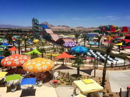 A vibrant water park with colorful umbrellas, slides, and palm trees against a clear blue sky and mountains in the background.