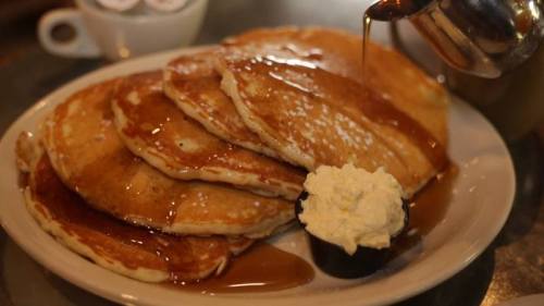 A stack of fluffy pancakes drizzled with syrup, topped with a dollop of whipped cream on a plate.