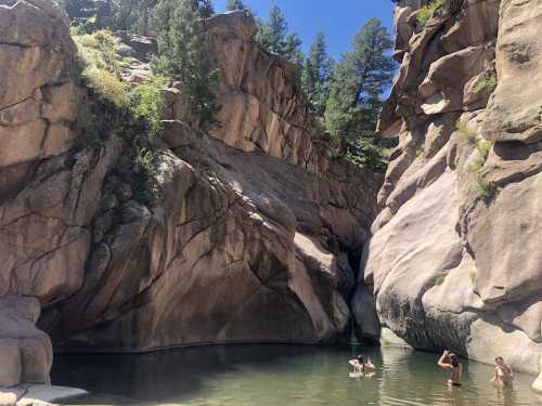 A serene natural pool surrounded by tall rock formations and trees, with people swimming in the water.