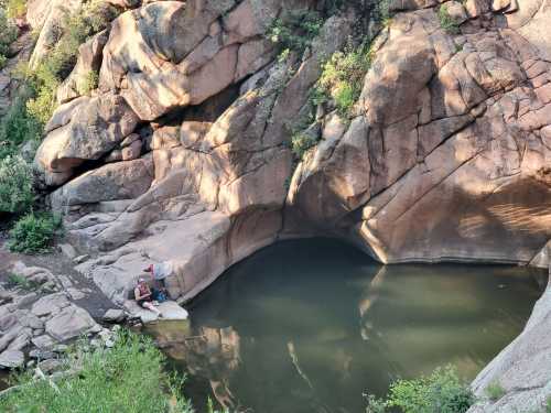 A serene rocky landscape with a small pool of water, surrounded by greenery and sunlight casting shadows.