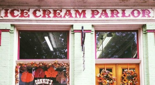 Sign for "Ice Cream Parlor" above a storefront with autumn decorations and large windows.