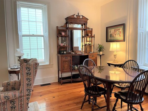 Cozy dining area featuring a wooden table, chairs, vintage cabinet, and natural light from large windows.