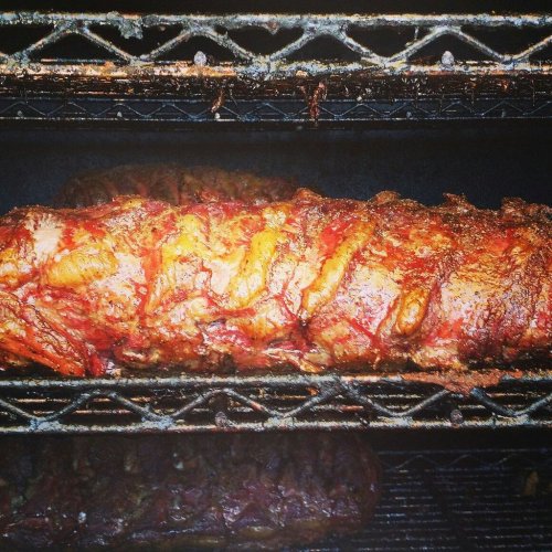 Close-up of smoked meat on a grill, showcasing a rich, caramelized exterior and juicy texture.