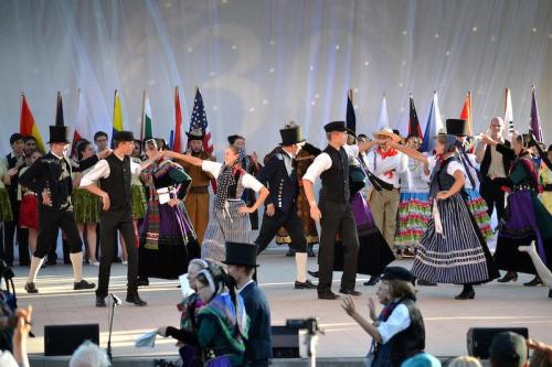 A lively dance performance featuring performers in traditional costumes on stage, with flags in the background.