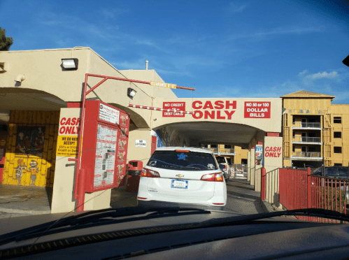 A car approaches a drive-thru with a "Cash Only" sign and instructions for payment. Bright blue sky in the background.