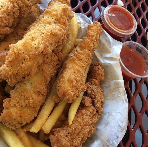 A plate of crispy fried chicken tenders served with golden fries and two small cups of dipping sauce.