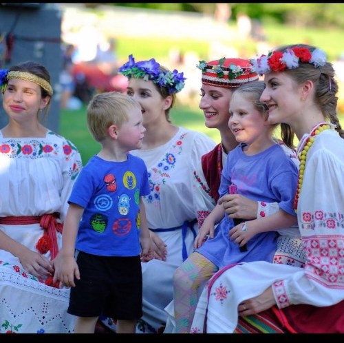 A group of children and women in traditional attire smiling and interacting at an outdoor event.