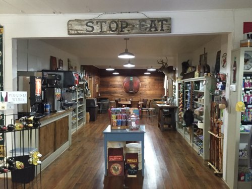 Interior of a rustic store with wooden decor, shelves of goods, and a dining area in the background. Sign reads "STOP EAT."