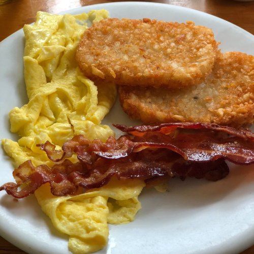 A plate with scrambled eggs, crispy bacon, and two golden hash brown patties.