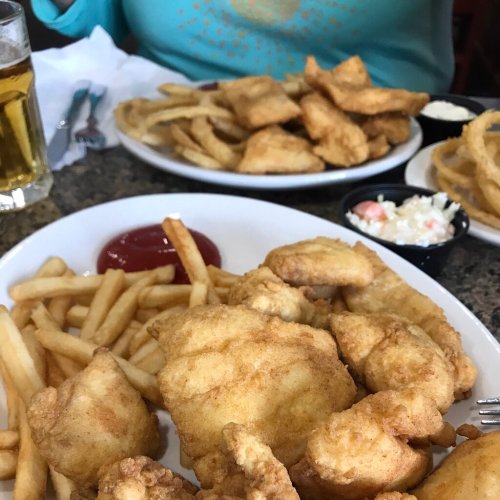 A plate of fried fish and French fries with ketchup, alongside a plate of onion rings and coleslaw in the background.