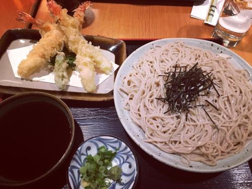 A plate of soba noodles topped with seaweed, accompanied by tempura shrimp and a dipping sauce, garnished with green onions.