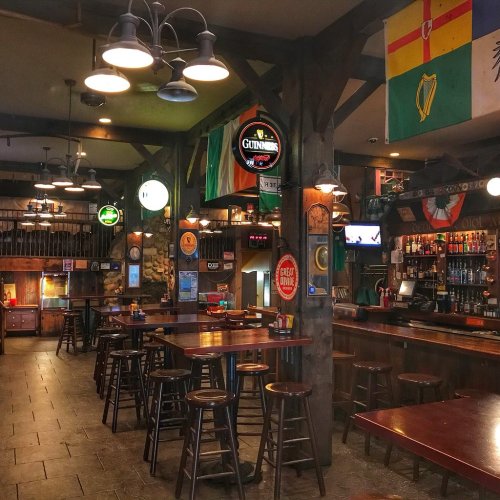 A cozy pub interior with wooden beams, bar stools, and various beer signs, featuring a warm, inviting atmosphere.