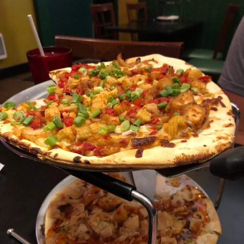 A close-up of a pizza topped with diced vegetables and green onions, served on a stand in a casual dining setting.