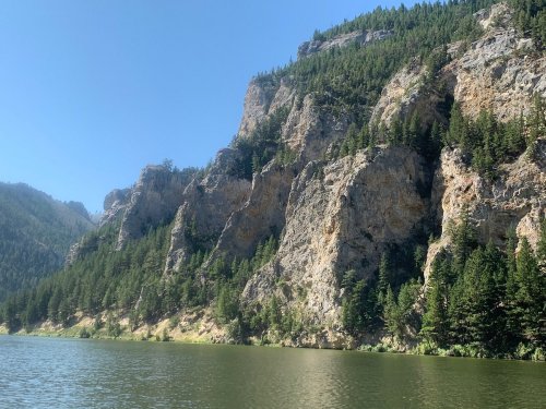 A serene lake surrounded by towering rocky cliffs and lush green trees under a clear blue sky.