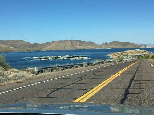 A scenic view of a winding road leading to a lake surrounded by hills under a clear blue sky.