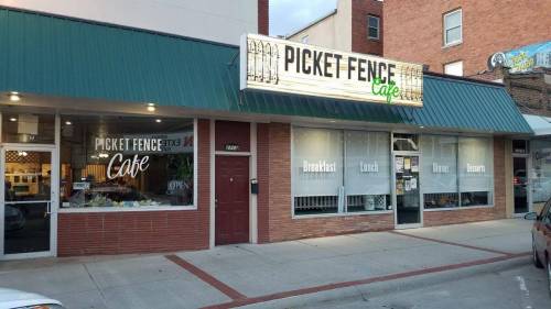 Exterior of Picket Fence Cafe, featuring a green awning and large windows displaying "Breakfast, Lunch, Dinner, Desserts."