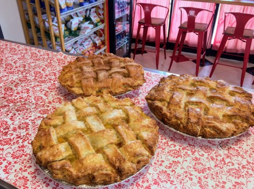 Three freshly baked pies with lattice crusts sit on a patterned tablecloth in a bright, inviting setting.
