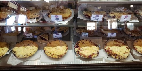 A display case filled with various fruit pies, including cherry, raspberry rhubarb, blueberry, and apple crumble.