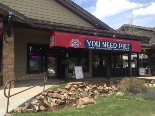 A diner with a red awning reading "YOU NEED PIE!" featuring outdoor seating and a landscaped entrance.