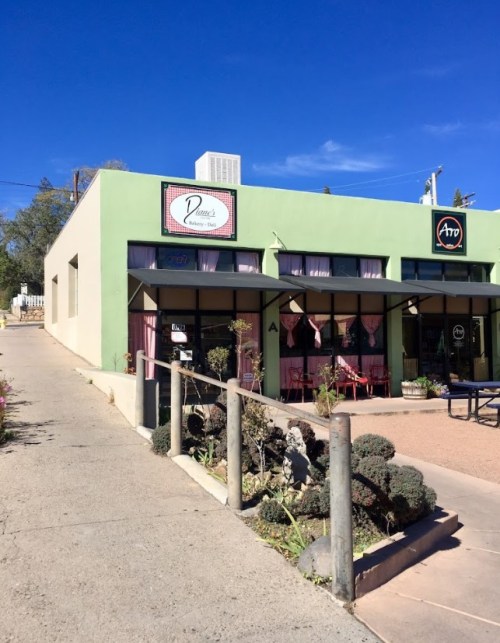 A green building with a sign for "Penny's Bakery" and pink curtains in the windows, set against a clear blue sky.