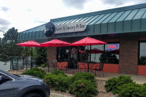 Exterior of Sweet & Savory Pi Bar with red umbrellas, outdoor seating, and an "OPEN" sign.