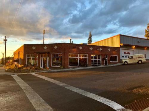 A brick building with large windows and a garage door, set against a sunset sky, on a quiet street.