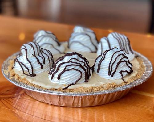 A pie with a graham cracker crust topped with whipped cream and chocolate drizzle, featuring six dome-shaped mounds.