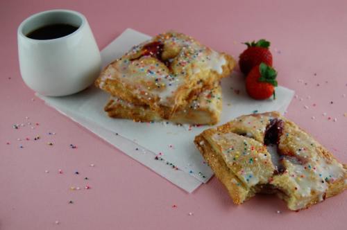 A plate of glazed pastries with sprinkles, fresh strawberries, and a cup of coffee on a pink background.