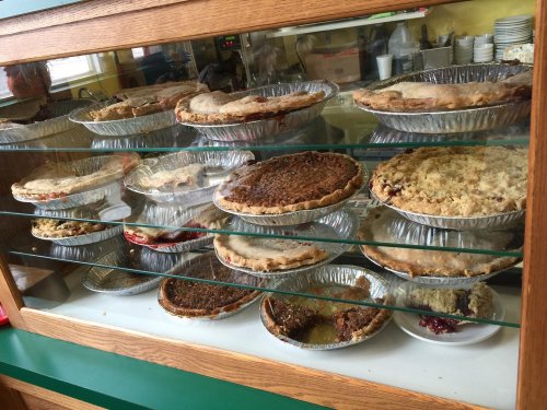 A display case filled with various pies in aluminum pans, showcasing different flavors and crusts.
