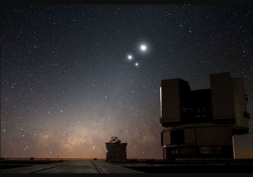 A starry night sky with two bright celestial bodies and an observatory structure in the foreground.