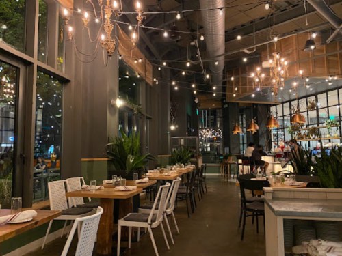A modern restaurant interior with wooden tables, stylish lighting, and greenery, creating a warm and inviting atmosphere.