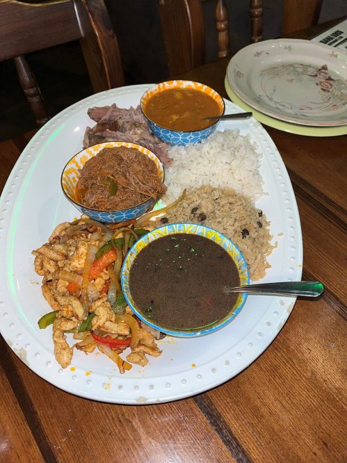 A platter with rice, beans, meat, and colorful sautéed vegetables in decorative bowls on a wooden table.