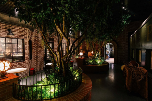 A dimly lit indoor space featuring brick walls, greenery, and decorative lighting elements.