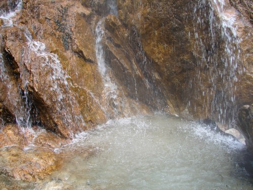 A close-up of a rocky waterfall, with water cascading over stones into a small, clear pool below.