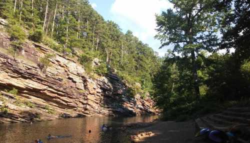 A serene river scene surrounded by rocky cliffs and lush green trees under a clear blue sky.