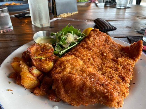 A plate of crispy fried fish with golden potatoes and a side salad, served with dipping sauce on a wooden table.